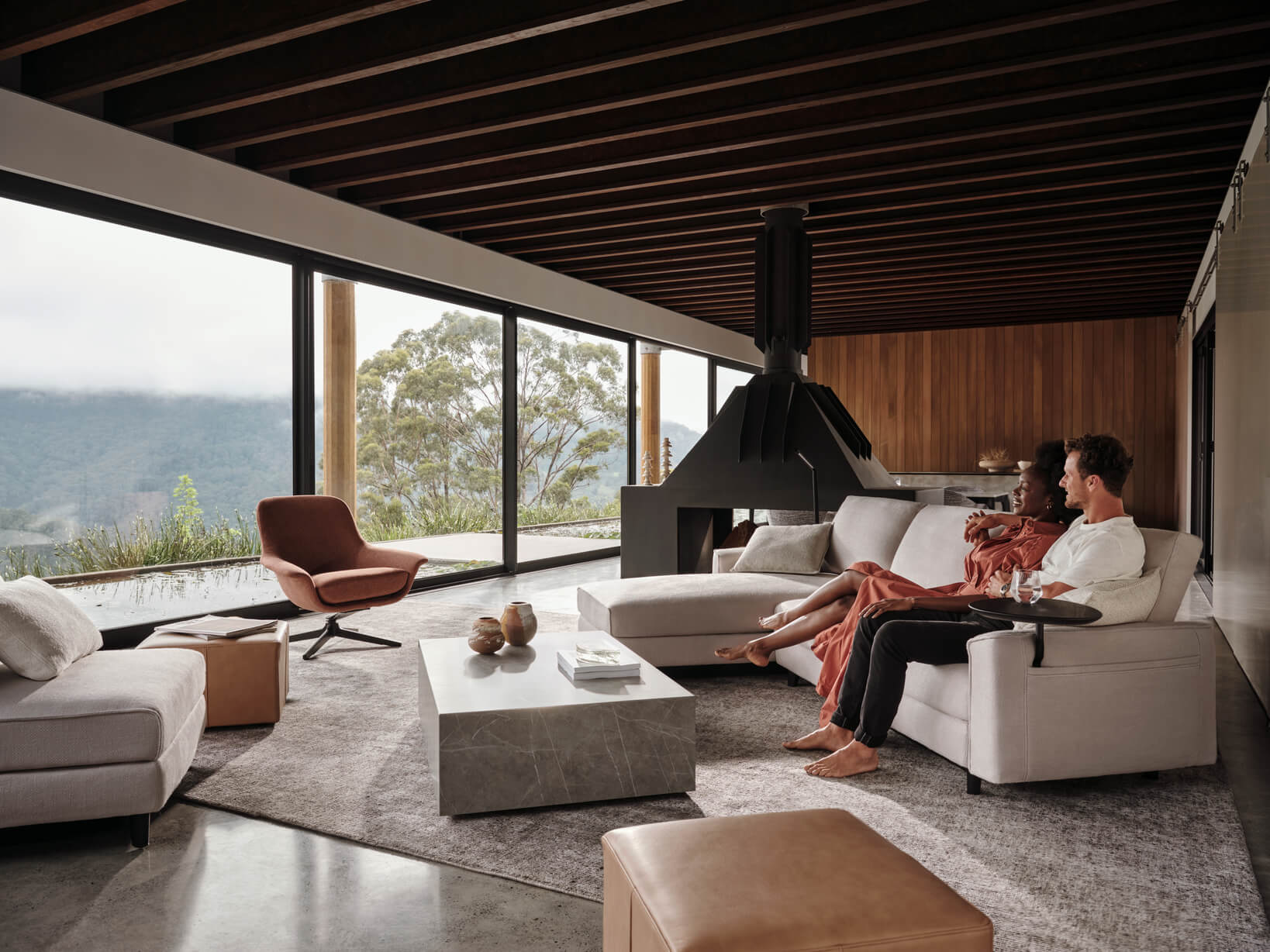 A couple relax on a contemporary, modular sofa in their home. The living room is warm and bright, minimally styled.